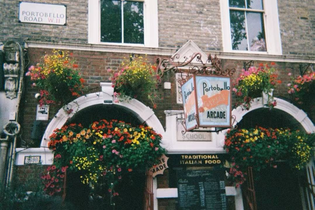 街角店铺的拱门挂满彩色鲜花，墙上可见 Portobello Road 路牌。